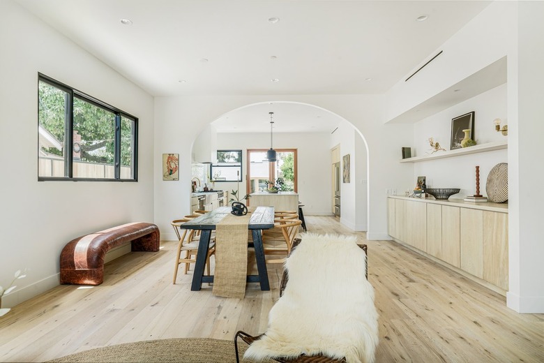 Dining room with a black dining table with beige table runner, brown leather accent bench, light wood sideboard and flooring