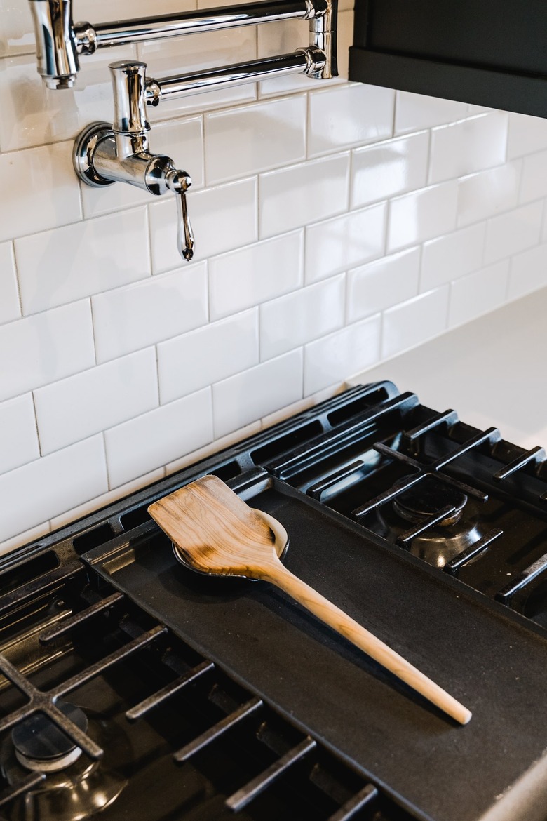 Stovetop with a wood utensil on a holder and a white tile backsplash with a pot filler faucet