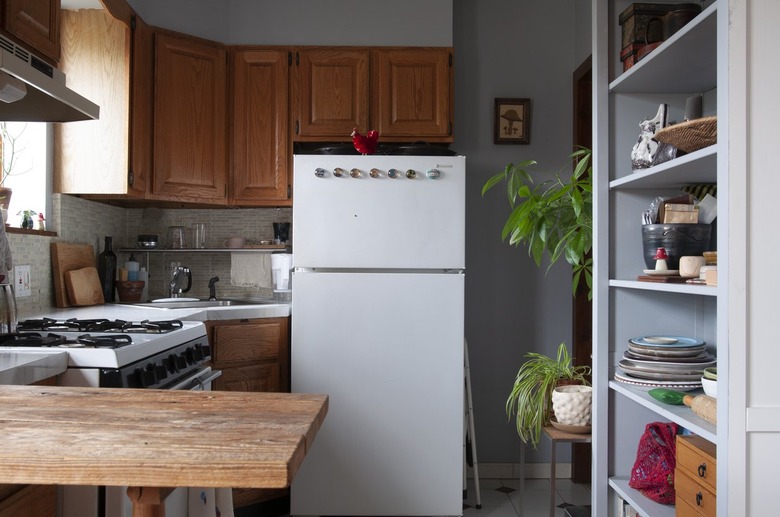 Kitchen with wood cabinets, white counters, gray tile backsplash, built-in shelve with dish ware, and plants.