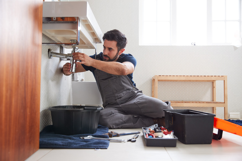 Male Plumber Working To Fix Leaking Sink In Home Bathroom