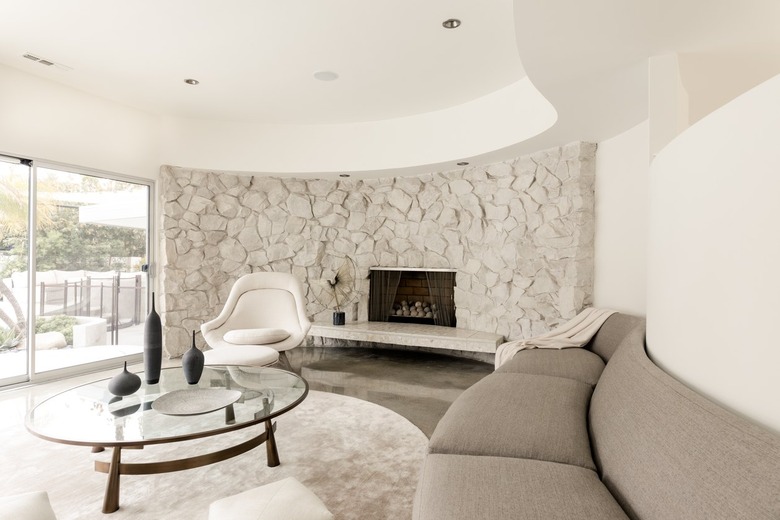 Living room with stone accent wall, fireplace, round coffee table with black vases, rounded sofa, rounded accent chair, and round rug