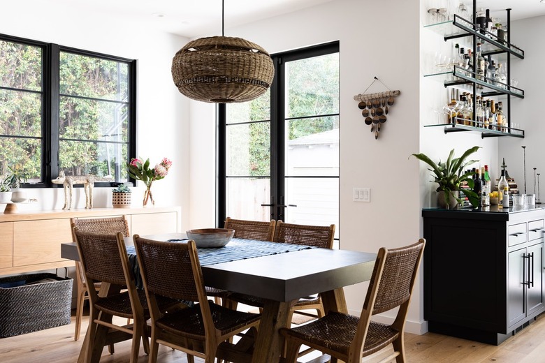 A dining room with a wicker globe pendant light, large windows and a bar