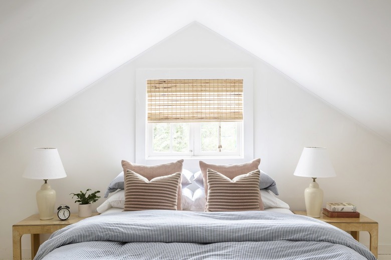 Bed with a blue pinstripe comforter and two matching blonde-wood end tables under a steeply sloping roof.