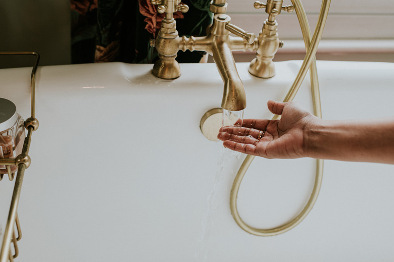 Checking the temperature of bath water under brass faucet.