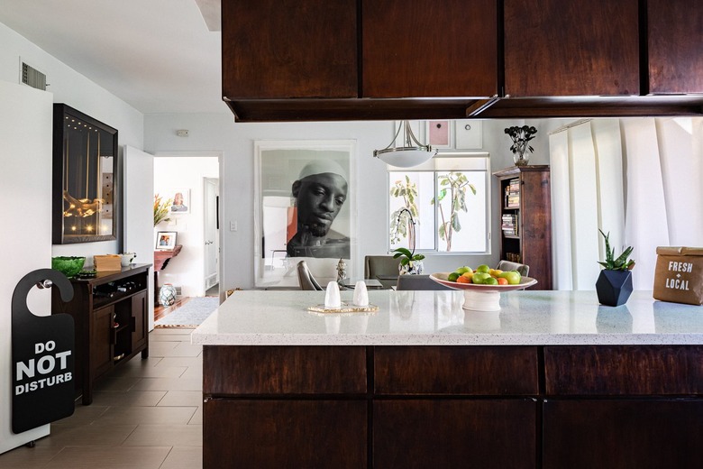 Kitchen with wood cabinets and white counters with accent dish ware, dining room with wood furniture and contemporary art.