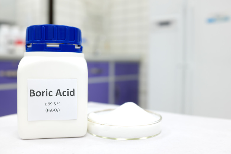 Selective focus of a bottle of pure boric acid chemical compound beside a petri dish with solid crystalline powder substance. White Chemistry laboratory background with copy space.