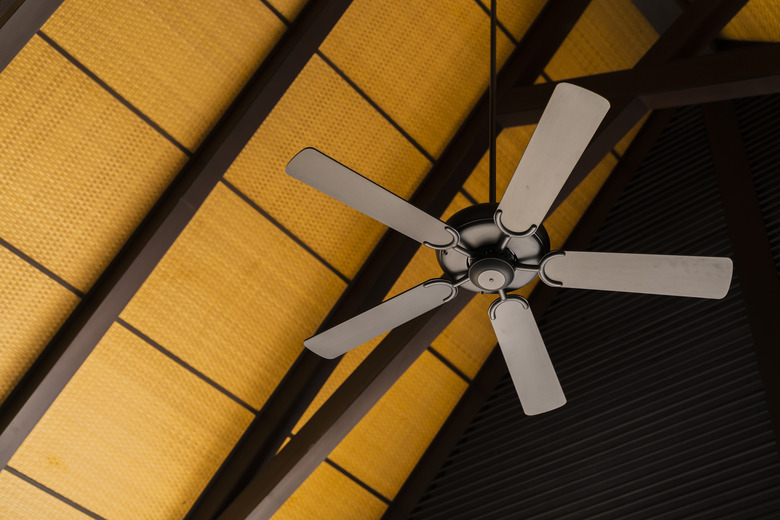 brown indoor ceiling fan on an exposed wooden support beam, with a decorate wooden ceiling, in the hall of living room of a contemporary home interior,home interior design concept