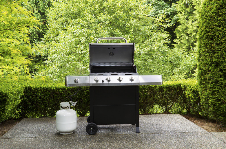 Large outdoor bbq cooker with white propane tank on home concrete patio