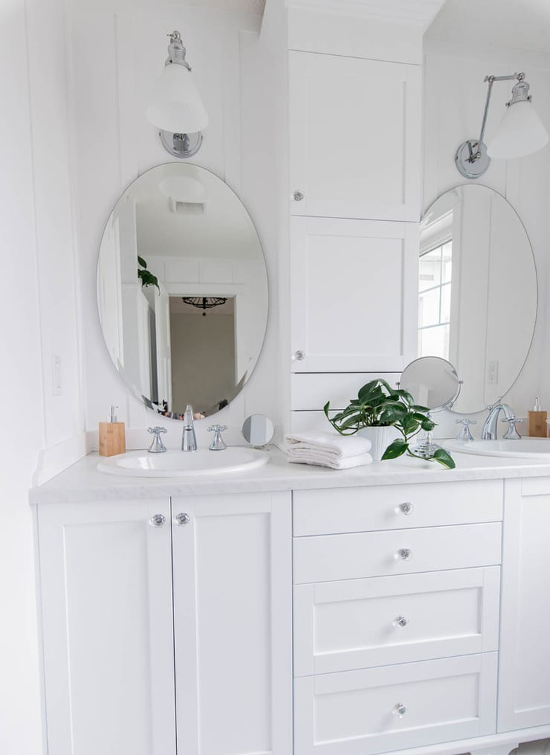 marble laminate bathroom countertop with white vanity cabinet and oval mirrors with wall sconces