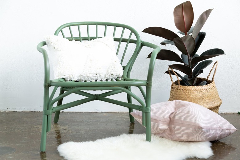 Green rattan chair with pillows, potted plant in basket, and sheep rug