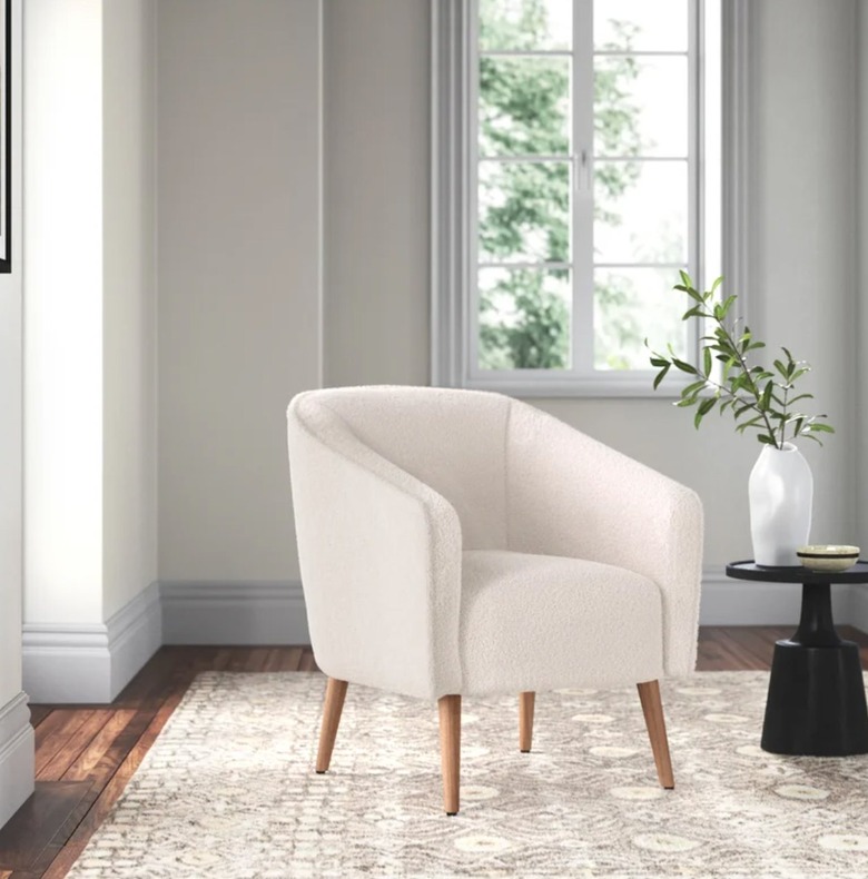 Off-white accent chair, rug, end table, vase.