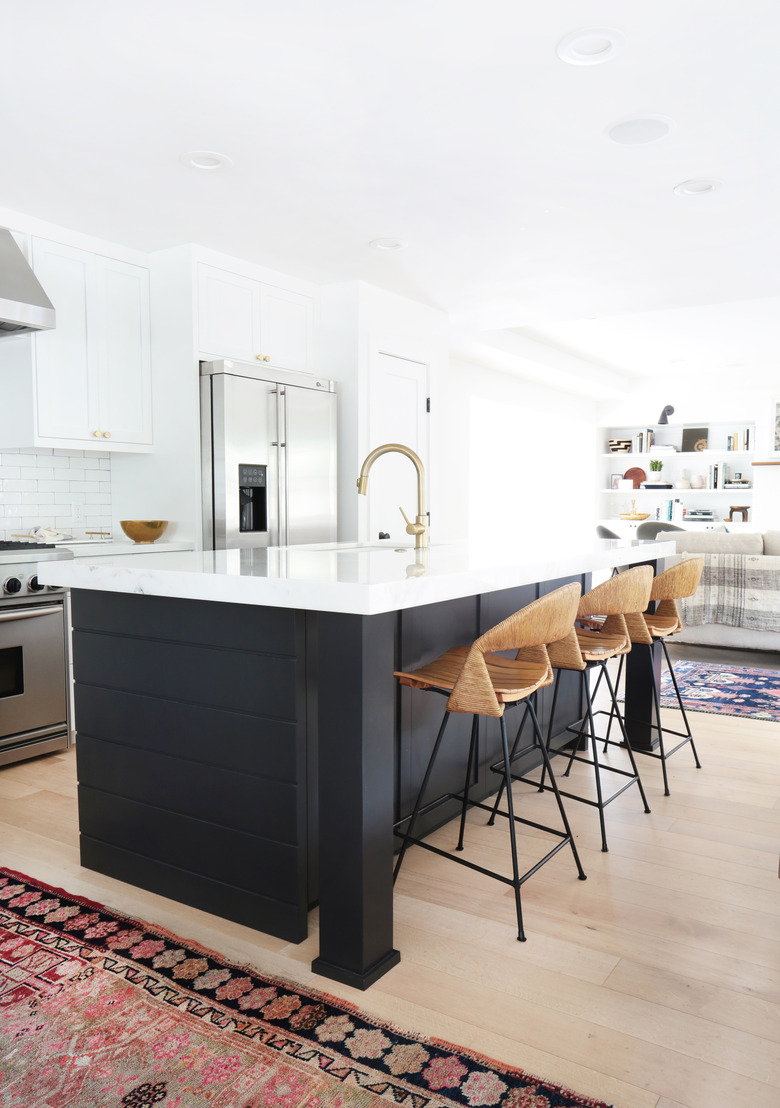 white kitchen with dark island and rattan chairs