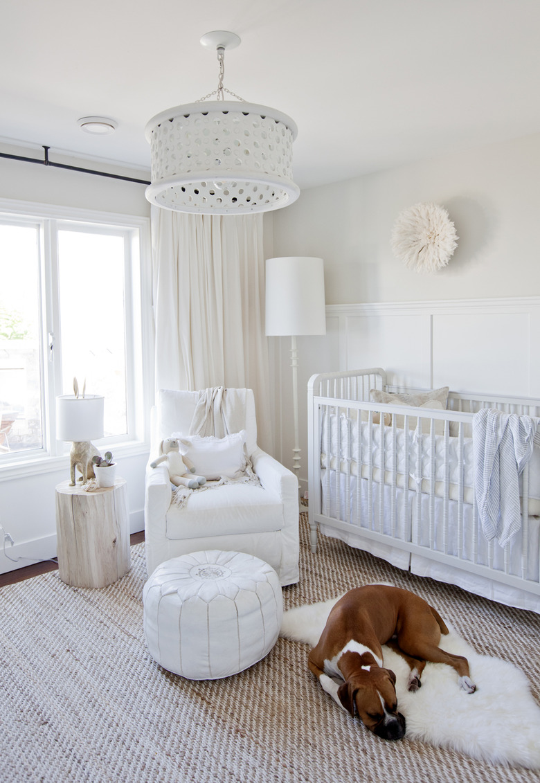 a neutral white nursery with upholstered rocker and sheepskin rug