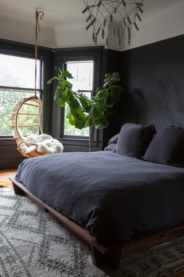 bedroom with matte black walls and black bedding with hanging chair in the window