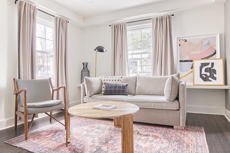 A living room with neutral furniture, a pink rug, and pink curtains over two windows