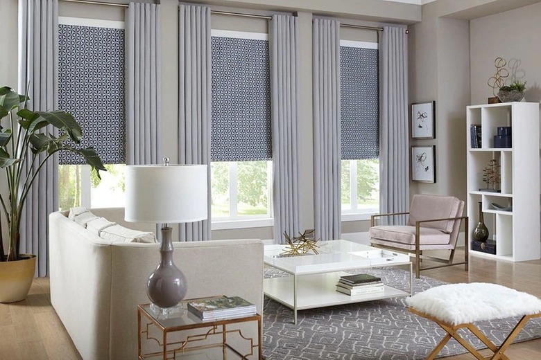 A living room with three windows covered with shades and curtains