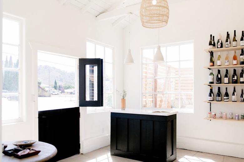 Wood shelves with bottles of wine, black casement door, white pendant lights, woven pendant shade, black and white bar.