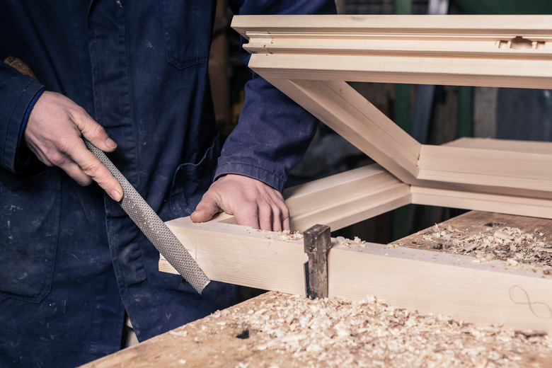 Carpenter Working on a Wooden Window Frame With a File