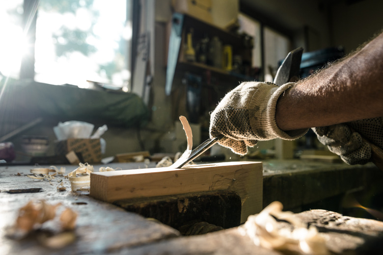 An experienced carpenter shapes wood with a chisel.