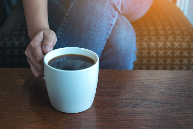 Closeup image of a woman's hand holding a cup of hot coffee to drink while sitting in cafe