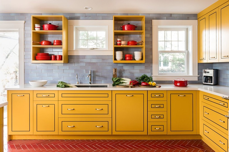 Bold kitchen with yellow cabinets, open shelving, red herringbone floor tiles and cool blue tile backsplash.