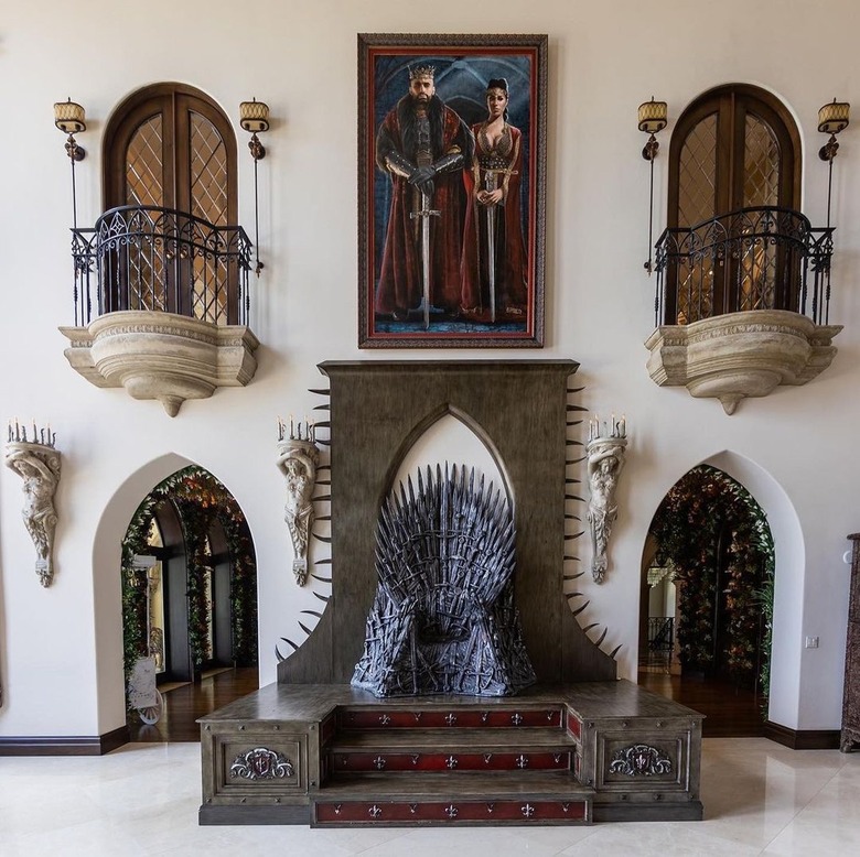 Game of Thrones Iron Throne underneath a painting, mirroring balconies, and mirroring doorways in front of a white wall.