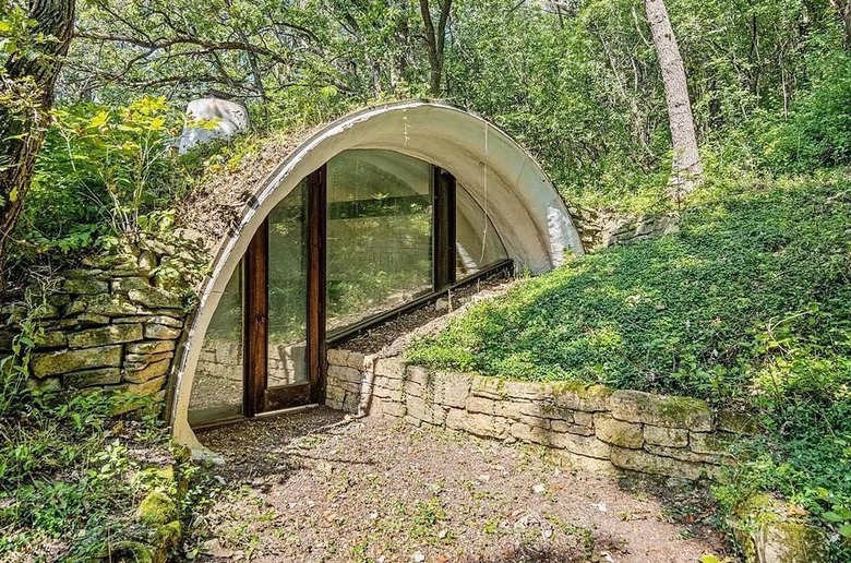 Exterior of a hobbit house building into greenery with an arched doorway.