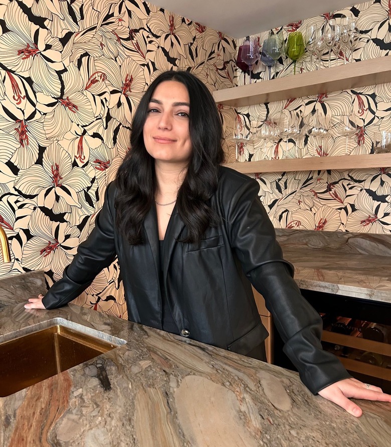 Zoya Biglary, a woman with long black hair, standing in front of a dark gray marble counter with a black leather jacket on.