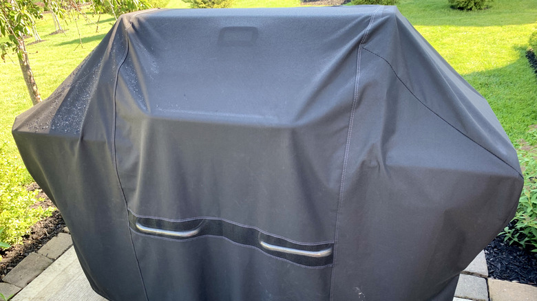 Grill with black cover on a cement patio with green lawn in the background