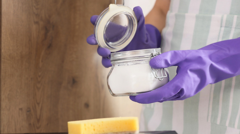 Person in purple protective gloves holding jar of baking soda mixture