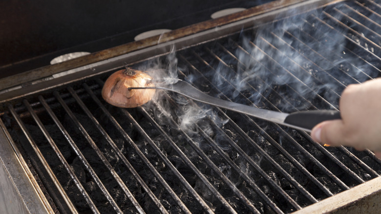 Person pressing a cut onion on a grill grate with a large fork