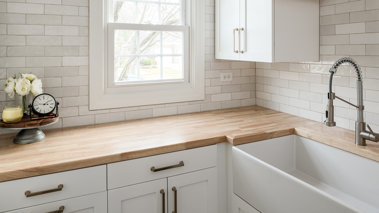 kitchen with creamy white cabinets, poliished nickel hardware, wood countertops, and varied tones of cream subway tile on the backsplash