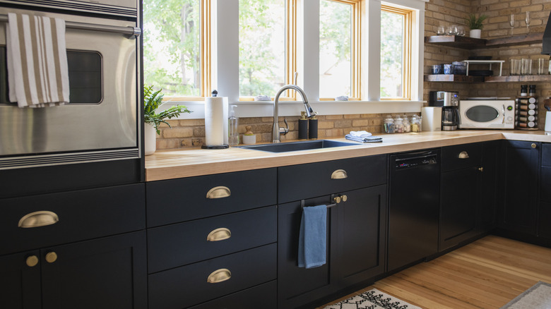 kitchen with black cabinets, light wood countertops, gold hardware, hardwood floors, and a brick backsplash