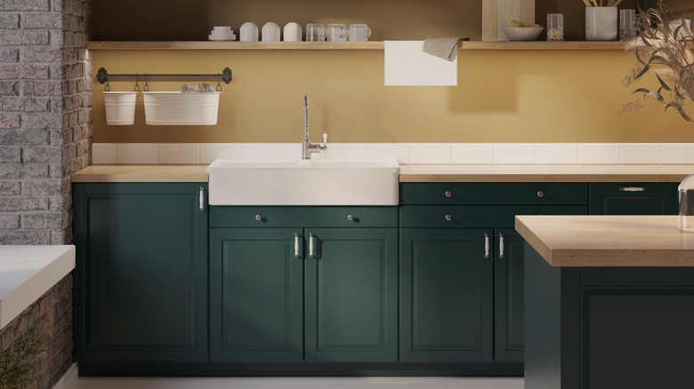 kitchen with dark green lower cabinets, light wood countertops, apron front white sink, polished nickel accents, exposed gray brick, and soft mustard yellow walls with open shelving