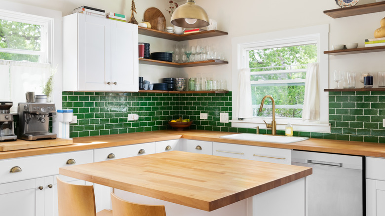 kitchen with white cabinets, emerald green subway tile backsplash, wood countertops, open wood shelving, and an island with two bar stools