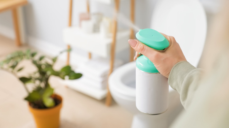 A woman's hand spraying air freshener near a toilet