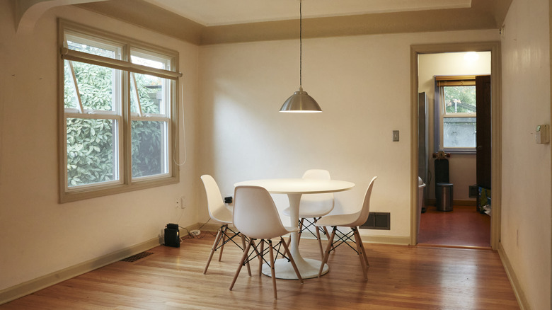 A small, bare dining room with a double-paned window. There is a small white tulip table in the middle with 4 midcentury dining chairs and a small gray light fixture above.