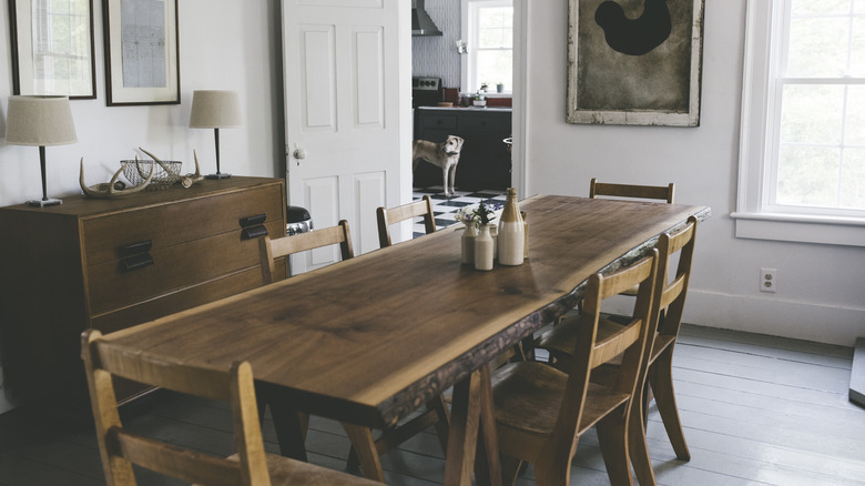 A minimalist dining room with white walls and matching wood table and chairs. There is some modern art and natural elements in the room.