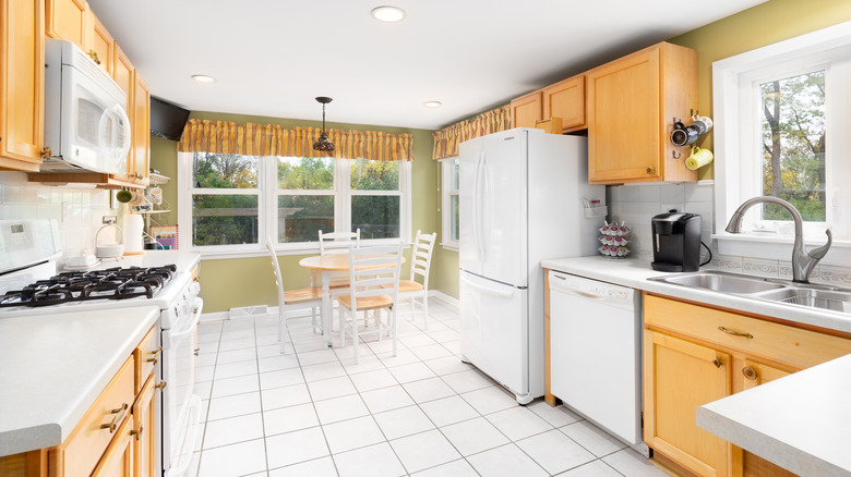 closeup photo of an out-of-date kitchen with oak cabinets, white tiles, and white appliances