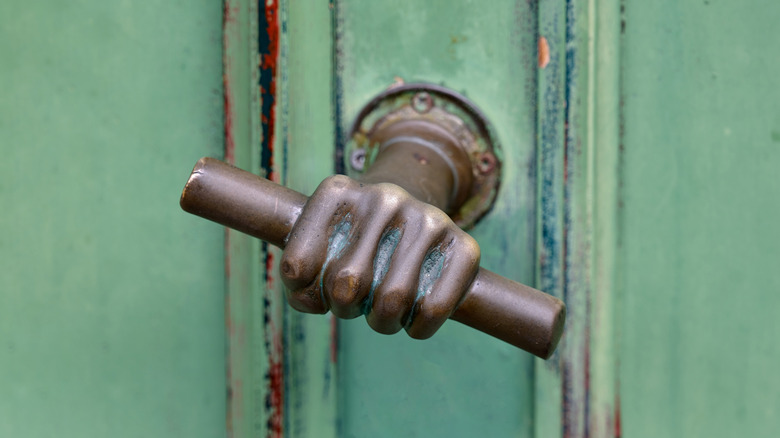 antique bronze door handle in the shape of a hand holding a tubular handle on a rustic green door