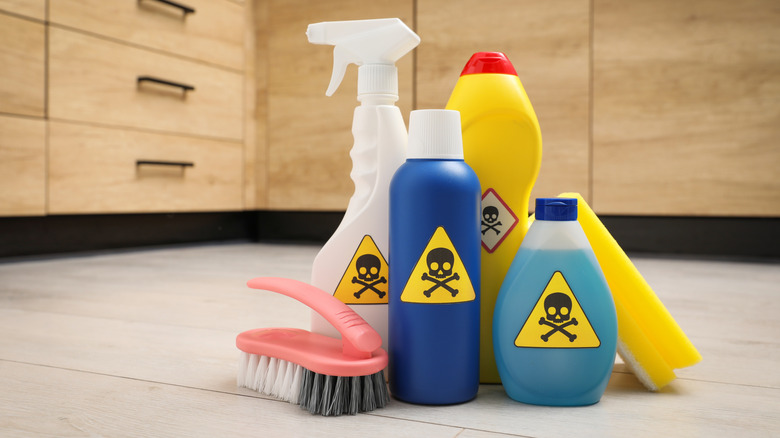 various cleaning supplies with toxic poison symbol on each of them, gathered together on the floor of a kitchen