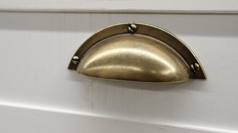 vintage-looking antique brass cup pull with exposed screws on a painted white cabinet drawer front