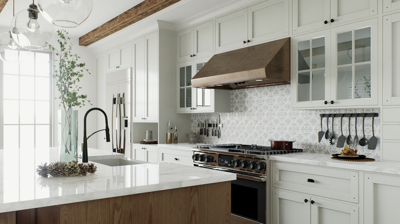 modern kitchen with off-white shaker perimeter cabinets, wood island, white stone countertops, wooden ceiling beams, and a patterned tile backsplash