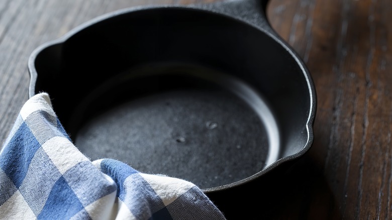 A close-up of a cast iron pan with a blue and white gingham towel resting on its edge.