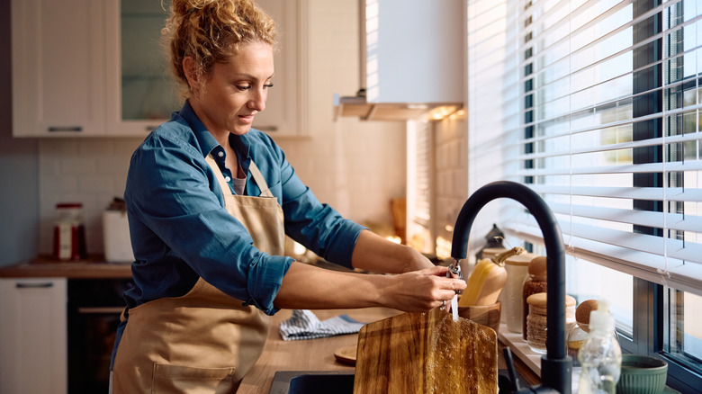 Person hand washing a wood cutting board in the sink