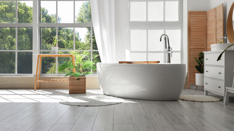 bathroom with tub, vanity, large windows in a minimalist natural design with wood looking floors