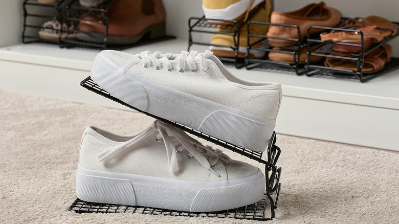 white sneakers with tall soles stacked up on a black wire IKEA SKOSTALL shoe organizer in front of a white closer shelf containing additional shoes lines up on the same organizers