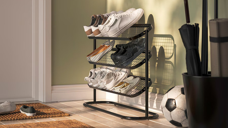 small corner by an entry door with a black IKEA ÄLGANÄS shoe rack filled with shoes