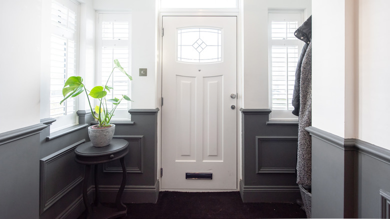 entryway with navy blue wall paneling, hanging coats, and table with potted plant