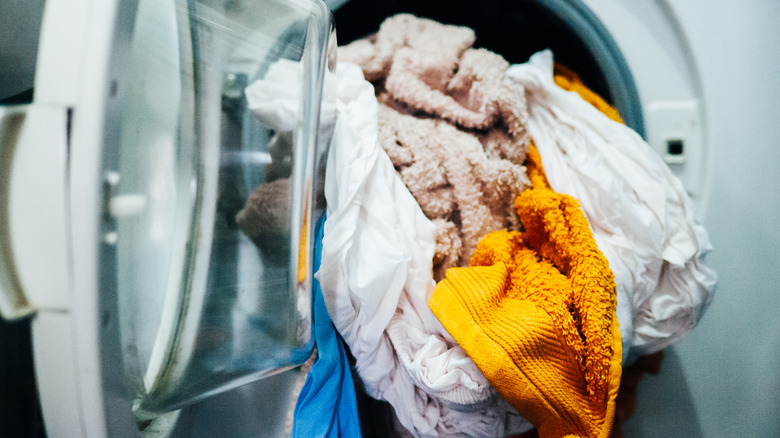 Wet laundry is tumbling out of a front-load washer door.